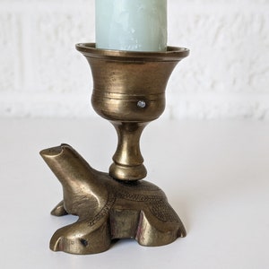 May include: A brass candle holder shaped like a turtle with a decorative design. The holder has a cup for a candle and a smooth, polished finish.
