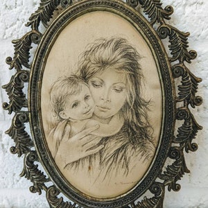 May include: A vintage oval-shaped framed drawing of a mother and child. The drawing is in black and white and depicts a woman holding a young child. The frame is ornate and has a gold finish.