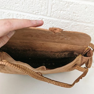 Puede incluir: Un bolso de cuero marr&oacute;n con detalles de costura amarilla. El bolso est&aacute; abierto y el interior es visible. El bolso tiene un cierre de solapa y una correa.