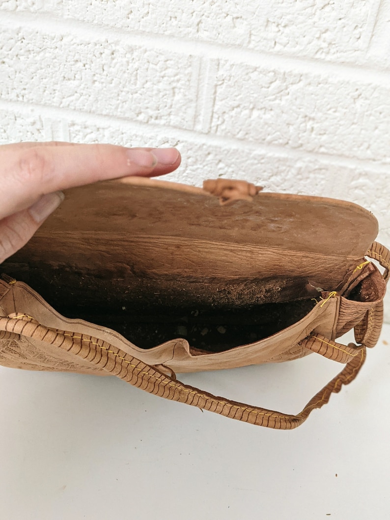 Puede incluir: Un bolso de cuero marr&oacute;n con detalles de costura amarilla. El bolso est&aacute; abierto y el interior es visible. El bolso tiene un cierre de solapa y una correa.