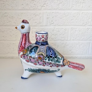 May include: A ceramic bird figurine with a candle holder. The bird is white with a red, blue, and green painted design. The bird has a long neck and a small head with a beak. The candle holder is on the bird's back.