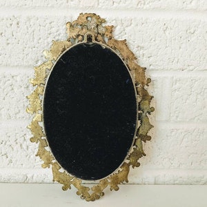 May include: An oval-shaped, gold-toned, ornate picture frame with a black velvet backing. The frame has a decorative, intricate design.