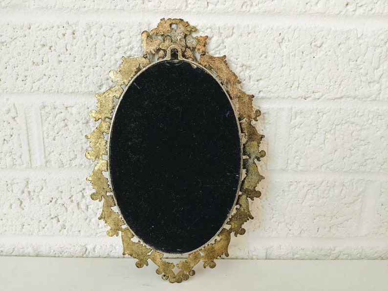 May include: An oval-shaped, gold-toned, ornate picture frame with a black velvet backing. The frame has a decorative, intricate design.