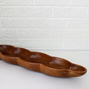 May include: A long, wooden serving bowl with a wavy, organic shape. The bowl is made of dark brown wood and has a smooth, polished finish.