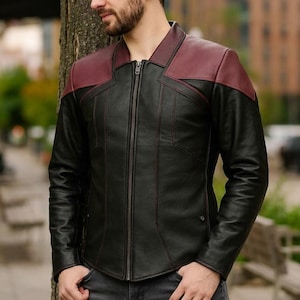 以下が含まれることがあります： 黒い革のジャケットで、肩にバーガンディのアクセントとフルレングスのジッパーが付いています。 ジャケットはクラシックな襟とテーラードフィットで、さまざまな場面に適しています。 ジャケットは革製です。