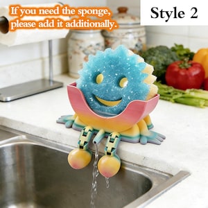 May include: A whimsical sponge holder in the shape of a smiling creature, with a blue sponge. The holder is pink and yellow, with blue arms and legs. The text "Style 2" is visible. The text "If you need the sponge, please add it additionally" is also visible.