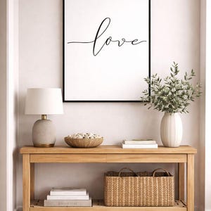 Könnte beinhalten: Eine Holzkonsolentisch mit einem gerahmten Druck mit dem Wort "love". Der Tisch ist mit einer Lampe, einer Schale mit dekorativen Objekten, einer Vase mit Grün, Büchern und einem Weidenkorb dekoriert. Der Raum hat eine neutrale Farbpalette.