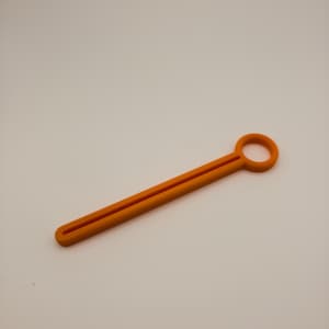 May include: An orange, elongated tool with a circular handle at one end and a slotted design along its length. The tool is made of a solid material and is set against a plain background.