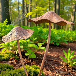 Op de afbeelding: Twee bronzen paddenstoel tuinpalen met getextureerde doppen en slanke stelen. Ze staan in een tuinbed met groen gebladerte en mos. De achtergrond toont een vage bosscène.