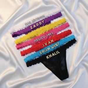 May include: A collection of colorful lace thong underwear with various names and phrases in silver lettering. The colors include white, purple, yellow, pink, red, blue, and black. The text includes "MRS EDGEMON", "ZADDY", "MEXICO 2024", "IVAN", "BRIAN WEST", and "KHALIL".