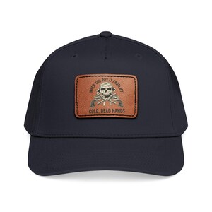 May include: Navy blue baseball cap with a brown leather patch featuring a skull, crossed pistols, and the text "WHEN YOU PRY IT FROM MY COLD, DEAD HANDS."