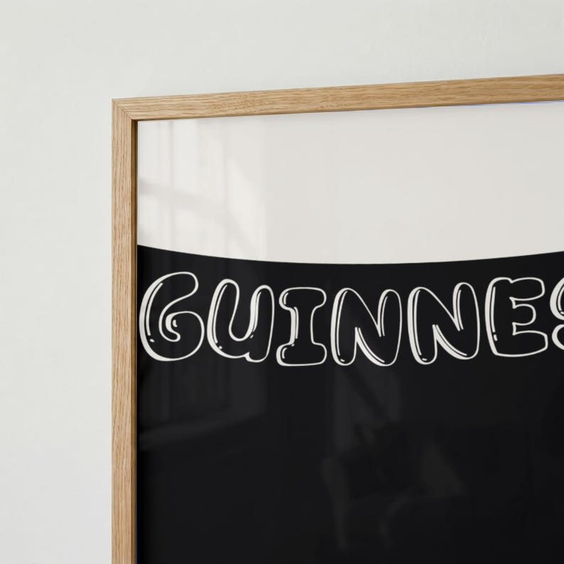 Puede incluir: Impresi&oacute;n enmarcada con la palabra "Guinness" en letras blancas redondeadas sobre un fondo negro. La parte superior es blanca y la impresi&oacute;n est&aacute; dentro de un marco de madera marr&oacute;n claro.