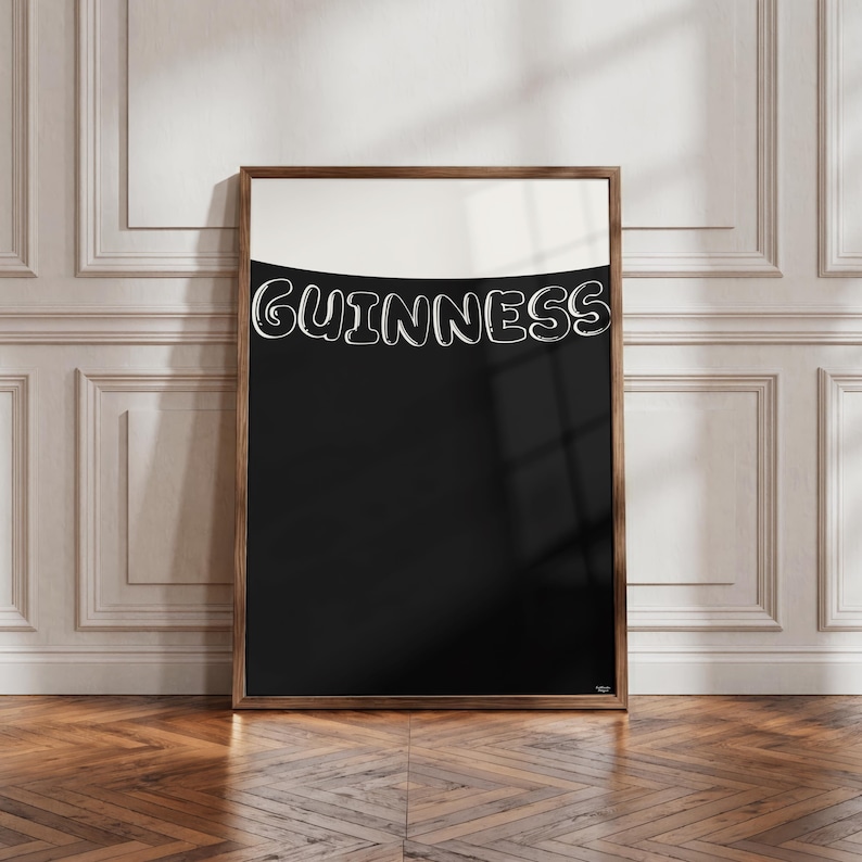 Puede incluir: Un cuadro enmarcado con el logotipo de Guinness en blanco sobre fondo negro. La parte superior es blanca, contrastando con el negro. El marco de madera le da un aspecto cl&aacute;sico. El cuadro est&aacute; sobre un suelo de madera.