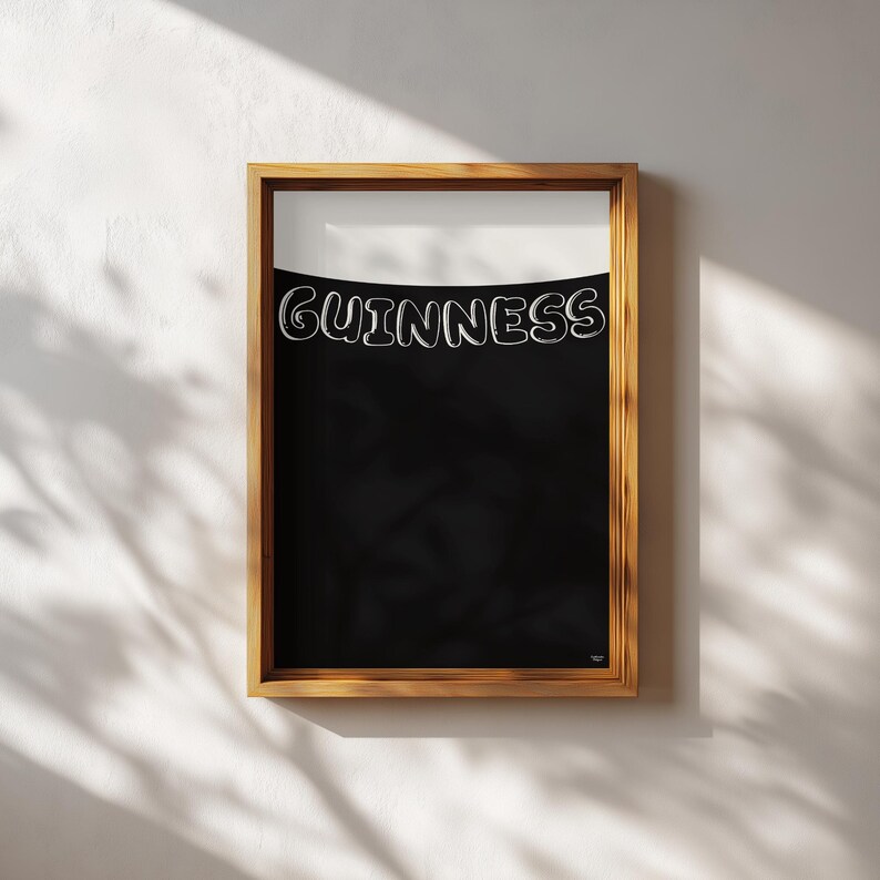 Puede incluir: Impresi&oacute;n enmarcada con el logotipo de Guinness en letras blancas curvadas sobre un fondo negro. La parte superior es blanca y el marco es de madera. La impresi&oacute;n est&aacute; colgada en una pared blanca, con sombras.