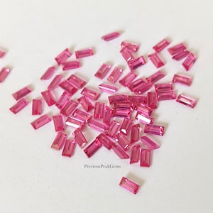 May include: A collection of small, rectangular, pink gemstones scattered on a white surface. The gemstones are a vibrant shade of pink and appear to be cut with precision. The image is well-lit, highlighting the facets of the gems.