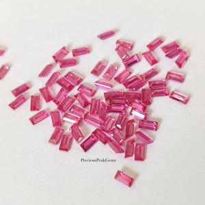 May include: A collection of small, rectangular, faceted pink gemstones arranged in a loose cluster. Each stone features a baguette cut with sharp edges and a vibrant magenta hue. The text PreciousPeakGems is printed in black at the bottom centre.