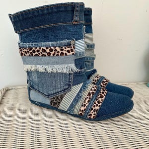Könnte beinhalten: Jeansstiefel mit Patchwork-Design. Die Stiefel bestehen aus verschiedenen Blautönen von Jeansstoff, akzentuiert mit Streifen aus Leopardenmuster-Stoff und Fransen. Ein einzigartiger, handgefertigter Modeartikel.