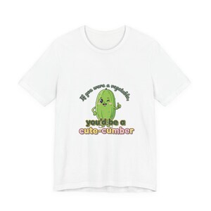 May include: White t-shirt featuring a cartoon cucumber with a smiling face and the text "If you were a vegetable, you'd be a cute-cumber". The cucumber is green with a light green outline. The text is in a playful font.