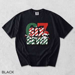 May include: A black short-sleeve t-shirt featuring a graphic print with the text SIX SEVEN. The design includes red and white candy cane stripes, green accents, and a Santa Claus figure wearing sunglasses and a hat, decorated with string lights.