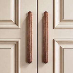 May include: Close-up of a cabinet door with two vertical, cylindrical wooden handles. The handles are a warm brown color, contrasting with the off-white cabinet door. The door has a recessed panel design with decorative molding.
