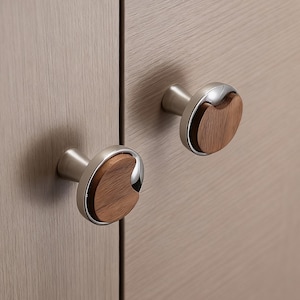Peut inclure: Deux boutons de meuble au design moderne. Chaque bouton est composé d'une base circulaire en métal brossé, d'un accent en métal poli en forme de croissant et d'un centre en bois. Les boutons sont montés sur une armoire en bois clair.