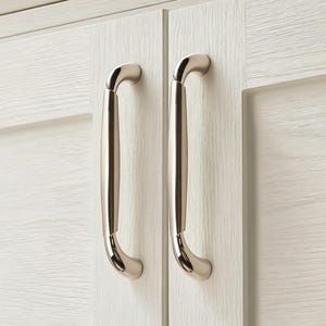 Op de afbeelding: Close-up van twee kastdeuren met handgrepen van geborsteld nikkel. De handgrepen zijn gebogen en gemonteerd op witte houten deuren met een getextureerde nerf. De kastdeuren staan naast elkaar.