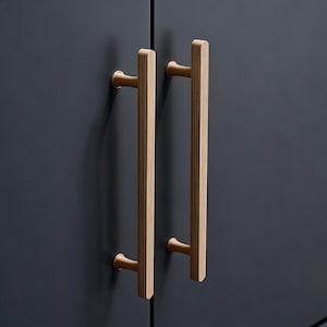 May include: Two vertical, light-coloured cabinet pulls with a ribbed design. The pulls are mounted on a dark blue cabinet door. The pulls have a cylindrical base and a rectangular handle. The hardware is made of metal.