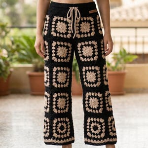 Puede incluir: Pantalones negros de ganchillo con un patrón cuadrado beige. Los pantalones tienen una cintura con cordón. La imagen muestra a una persona usando los pantalones. Los pantalones son un artículo único, hecho a mano.