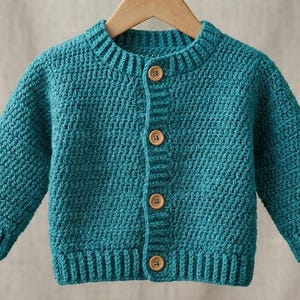 May include: Teal-colored crochet cardigan with a ribbed collar, cuffs, and hem. The button-down sweater features four wooden buttons and is displayed on a wooden hanger. The garment is made of a textured yarn.