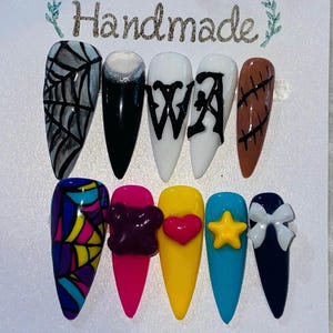 Puede incluir: Juego de uñas hechas a mano con varios diseños. Incluye una telaraña negra y gris, uñas negras con purpurina plateada, uñas blancas con letras negras y diseños coloridos con adornos.