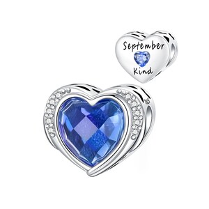 Könnte beinhalten: Ein herzförmiger Charm-Anhänger mit einem großen, facettierten blauen Edelstein in der Mitte, umgeben von einem silbernen Rahmen mit kleinen, klaren Steinen. Ein kleinerer Herz-Charm mit den Worten "September Kind" und einem blauen Edelstein.