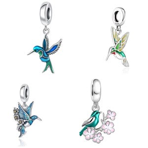 Pode incluir: Quatro berloques de prata com designs de beija-flores e pássaros com detalhes em esmalte colorido. Cada berloque inclui uma argola circular marcada com 925, exibindo figuras detalhadas de pássaros em tons de azul, verde e amarelo, alguns com flores.