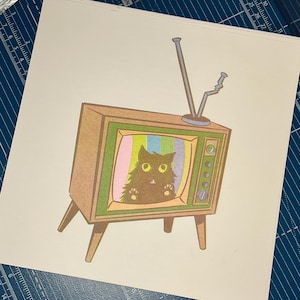 May include: A vintage-style illustration of a brown television set with a cat inside the screen. The TV has a wooden frame, green and pink accents, and a metal antenna. The cat has big yellow eyes and is looking out from the screen.
