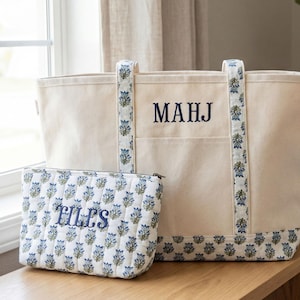 May include: A cream-colored tote bag and matching cosmetic bag. The tote features navy blue embroidered initials "MAHJ" and floral patterned trim. The cosmetic bag is quilted with a floral pattern and the embroidered word "TILES".