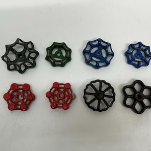 May include: Eight vintage water valve handles in various colors, including green, blue, red, and black. The handles have different spoke designs and are made of metal. They are arranged on a white surface.