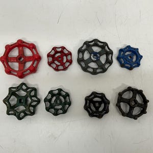 May include: A collection of eight vintage valve handles in various sizes and colors. The handles are red, dark red, blue, and shades of green and black. The handles have a circular design with spokes.