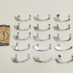 May include: Fifteen polished chrome door pulls arranged in five rows of three, each featuring a curved design with two attached mounting screws. A rectangular paper packaging sleeve is included, labeled No. 83418 DOOR PULL for Cabinet Parts.
