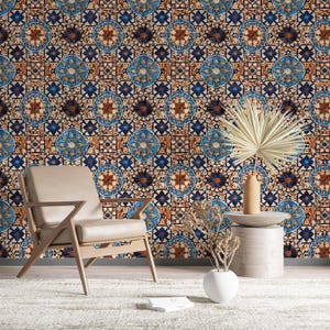 Op de afbeelding: Een kamer met behang met blauwe, bruine en witte geometrische patronen. Een beige fauteuil, een kleine bijzettafel en decoratieve items zoals een vaas en gedroogde planten zijn aanwezig. De vloer is bedekt met een wit tapijt.