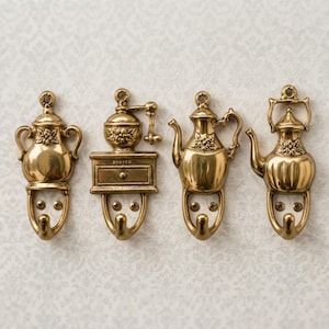 Puede incluir: Un juego de cuatro ganchos de pared de latón con diseños decorativos de temática de cocina. Cada gancho incluye una base de metal con forma de molinillo de café o tetera con detalles florales y un gancho curvo en la parte inferior.