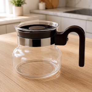 May include: A clear glass coffee carafe featuring a dark brown plastic lid and a matching dark brown handle. The carafe includes a polished silver-tone metal band encircling the upper section, connecting the handle to the main glass body.