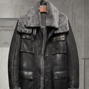 Könnte beinhalten: Ein langer schwarzer Ledermantel mit einem dicken grauen Lammfellkragen und Innenfutter. Der Mantel verfügt über vier Vordertaschen mit Klappen und Metalldruckknöpfen, einen zentralen Reißverschluss sowie Ärmelbündchen mit Lammfellbesatz.