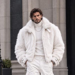 Puede incluir: Una chaqueta de piel sintética blanca con cuello alto, hebillas plateadas en los puños y cremallera frontal. La chaqueta se lleva sobre un suéter de cuello alto blanco y pantalones cargo blancos con bolsillos laterales, creando un conjunto blanco.
