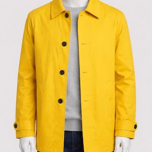 Puede incluir: Chaqueta amarilla brillante con cuello clásico y cierre de botones. La chaqueta tiene mangas largas con puños abotonados y dos bolsillos delanteros. El maniquí también lleva un jersey gris y vaqueros azules.