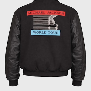 Puede incluir: Chaqueta bomber negra con mangas de cuero negro. La parte trasera de la chaqueta presenta el texto "MICHAEL JACKSON" en rojo, un gráfico de un bailarín y "WORLD TOUR" en azul.