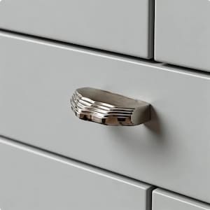 May include: A close-up of a gray cabinet with a silver, ridged drawer pull. The drawer pull is a half-oval shape with horizontal ridges. The cabinet is a light gray color.