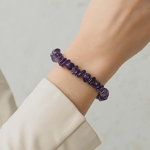 Peut inclure: Un bracelet composé de morceaux d'améthyste violets. Le bracelet est fait de petites pierres d'améthyste de forme irrégulière. Les pierres sont d'un violet profond et riche. Le bracelet est porté au poignet.