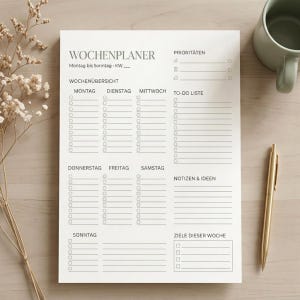 Könnte beinhalten: Ein weißer Wochenplaner mit deutschem Text, einschließlich "Wochenplaner" und Wochentagen. Er enthält Abschnitte für Prioritäten, To-Do-Listen, Notizen und Wochenziele. Ein goldener Stift und eine Tasse befinden sich auf der Holzoberfläche.