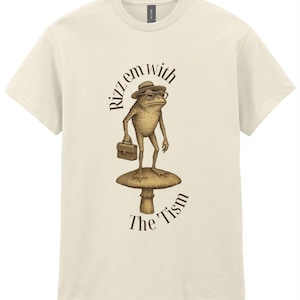Könnte beinhalten: Cremefarbenes T-Shirt mit einer skurrilen Illustration einer Froschfigur mit Hut und Brille, die einen Aktenkoffer hält und auf einem Pilz steht. Der Text "Rizz em with The Tism" ist um den Frosch herum angeordnet.