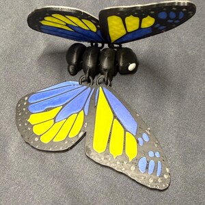 May include: A decorative butterfly with black, yellow, and blue wings. The butterfly has a black body and is designed with intricate details. The wings are open, showcasing the vibrant colors and patterns. The butterfly is a decorative item.