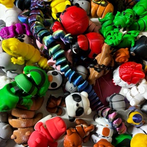 May include: A collection of colorful 3D-printed toys, including ladybugs, frogs, and a panda. The toys are in various colors such as red, green, yellow, and blue. A rainbow-colored articulated snake toy is also present.